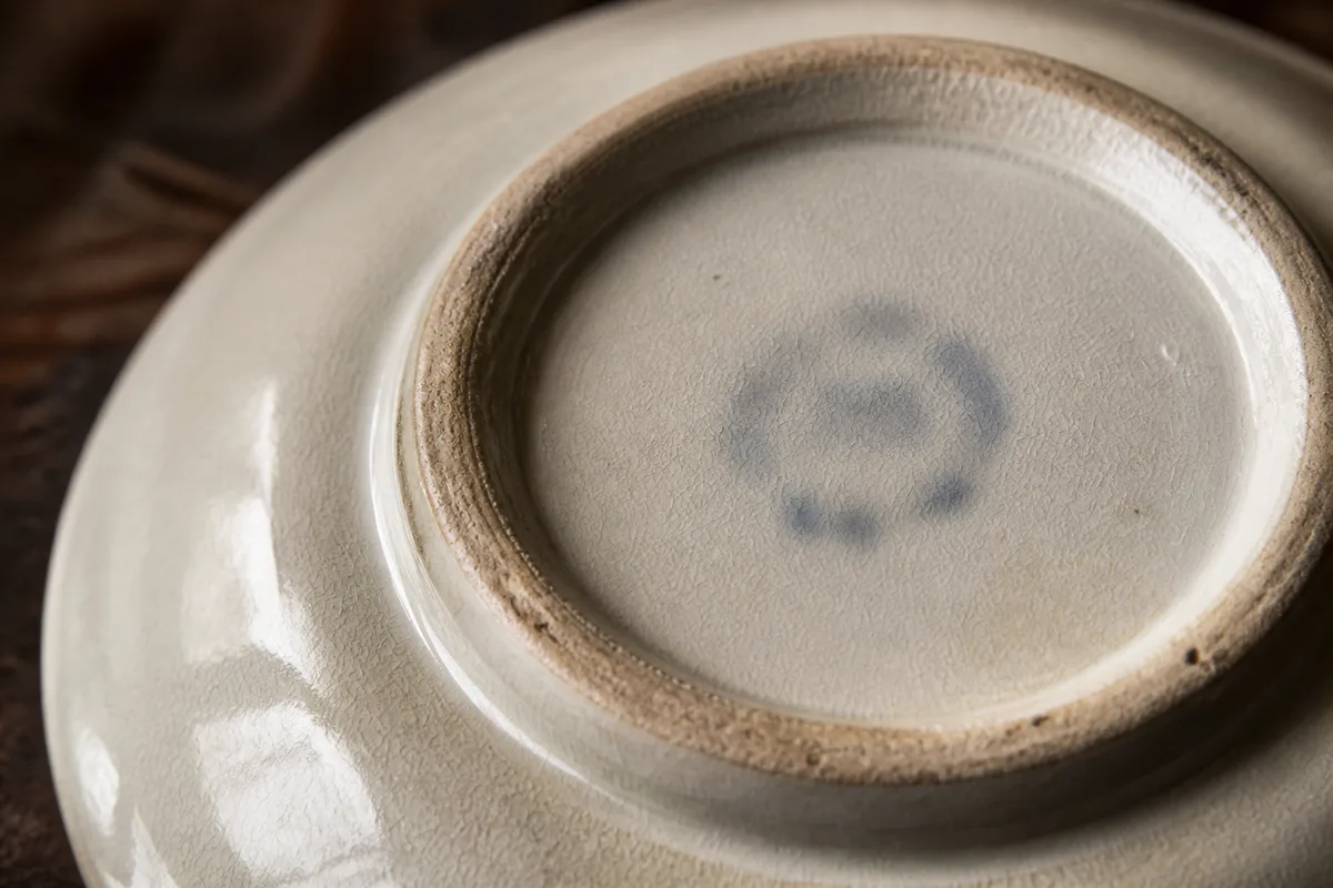 Assiette en faïence ancienne retournée montrant le pied non émaillé et sa marque de fabrique